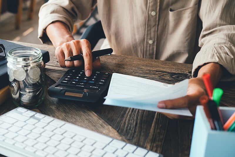 A person sits at a desk using a calculator while holding a sheet of paper